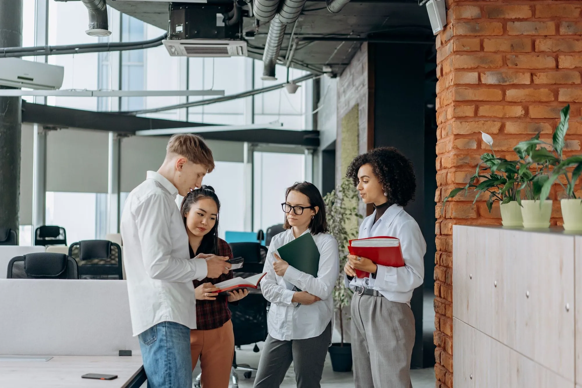 Four young colleagues with notebooks chatting in a modern loft office