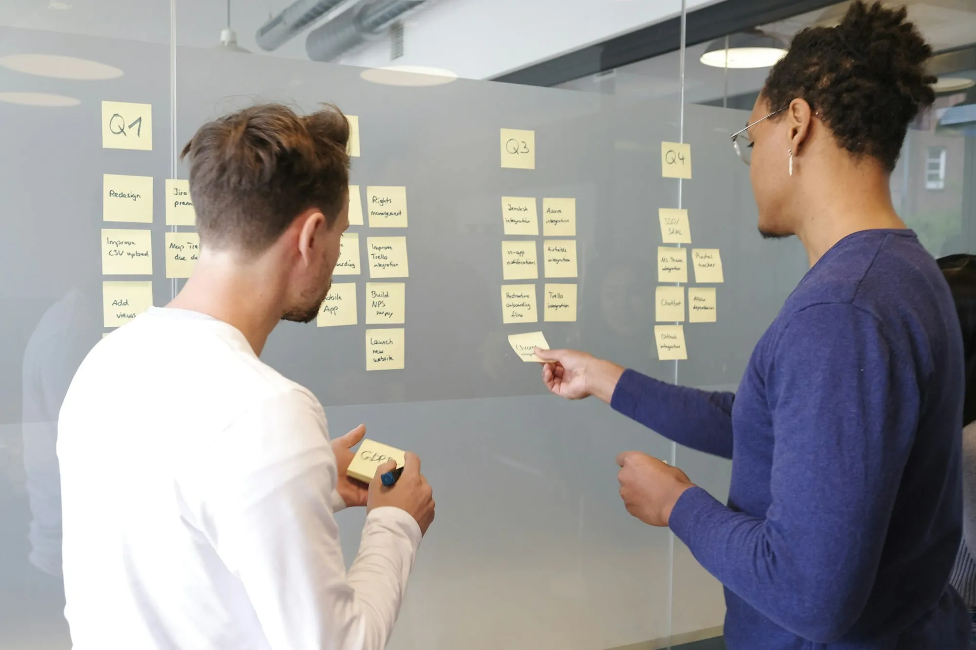 Two colleagues arranging sticky notes on a glass wall planning board